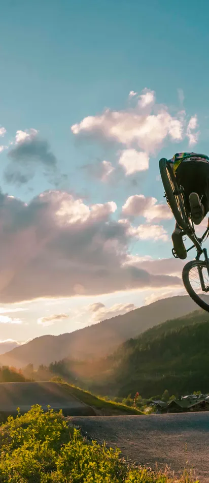 Mountainbiker springt bei Sonnenuntergang vor alpiner Landschaft