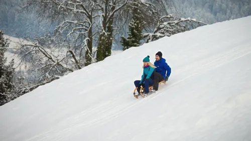 Paar rodelt eine verschneite Piste im winterlichen Wald hinunter