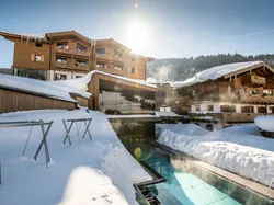 Luxuriöses Alpenhotel mit beheiztem Außenpool und Schnee in winterlicher Sonnenstrahlung