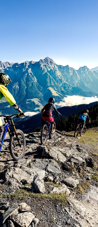 Mountainbiker fahren bergab auf felsigem Alpentrail mit Panoramablick auf die Berge