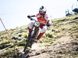 Downhill mountain biker racing on rocky trail wearing red gear and helmet with GoPro