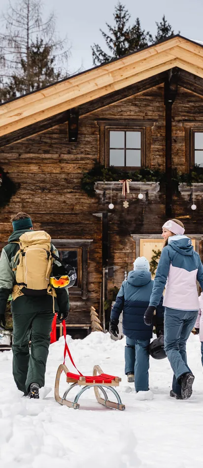 Familie zieht Schlitten durch den Schnee zu einer rustikalen Berghütte