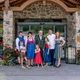 Family in traditional attire standing in front of hotel entrance with flowers and stone wall