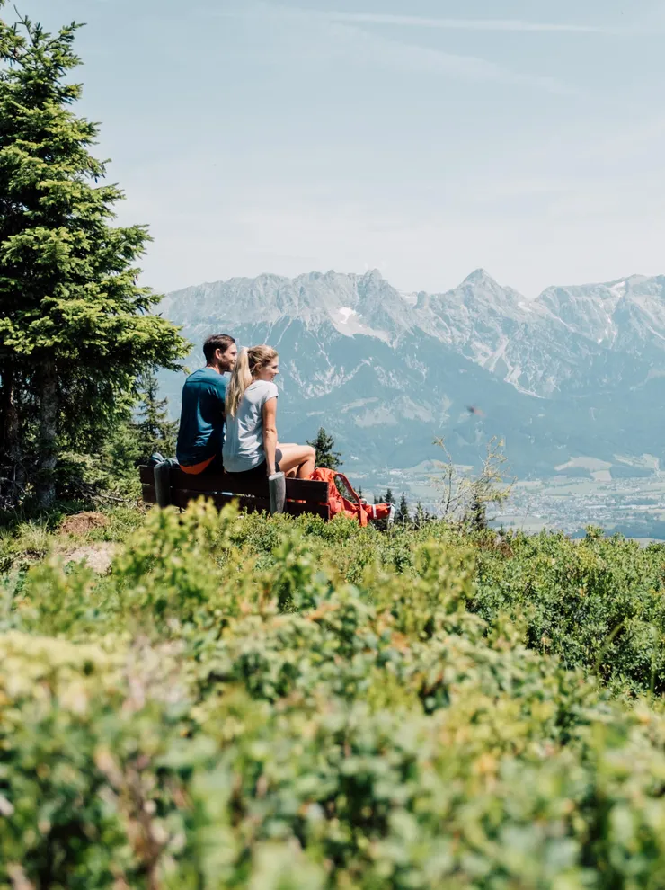 Couple sitting on mountain bench enjoying scenic alpine landscape with panoramic valley view