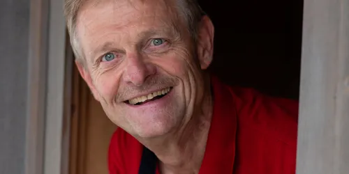 Lächelnder älterer Mann im roten Poloshirt lehnt sich aus Holzfenster