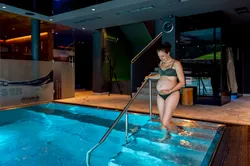 Schwangere Frau im Bikini steigt in den Innenpool eines Wellnessresorts