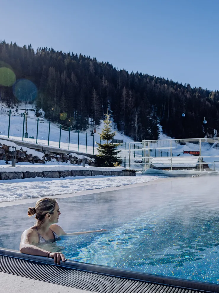 Woman relaxing in outdoor heated pool with snowy alpine mountain view