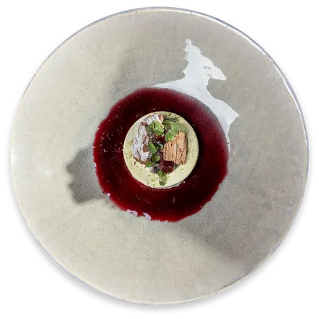 Gourmet-Dessert mit grünem Mousse, roter Beerensauce und essbarer Garnitur auf Keramikteller