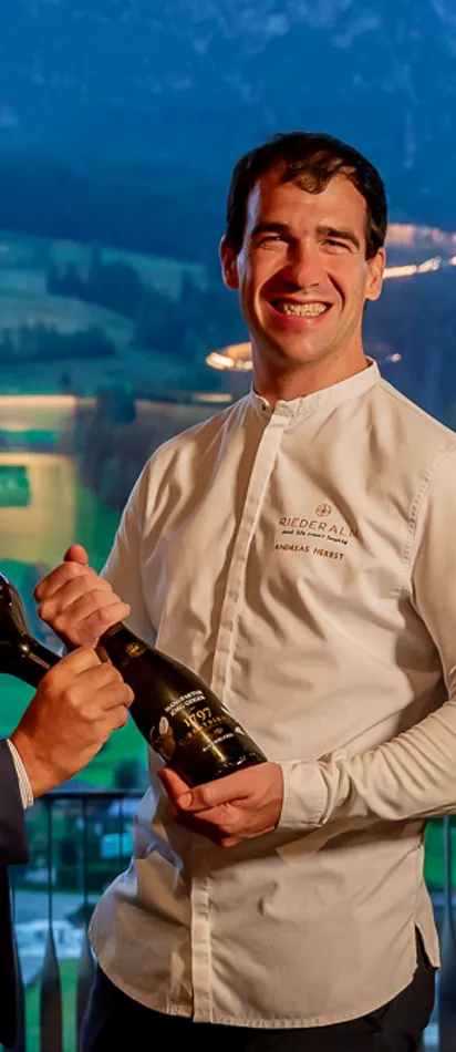 Drei Männer in Gourmetrestaurant mit Weinflaschen und Bergblick im Hintergrund