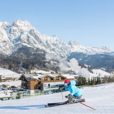 Skier carving on groomed slope with snowy Alpine mountains and chalets in background