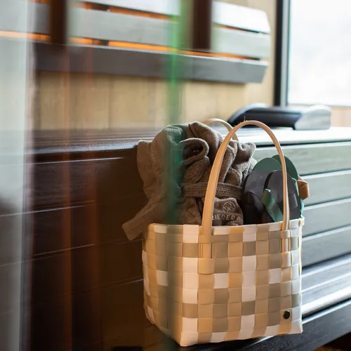 Geflochtener Korb mit Handtüchern und Flip-Flops auf hölzerner Saunabank