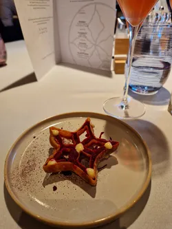 Gourmet star-shaped dessert with berry sauce and cream dots on a beige plate