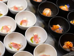 Assorted gourmet appetizers in white and black bowls with raw fish and edible flowers