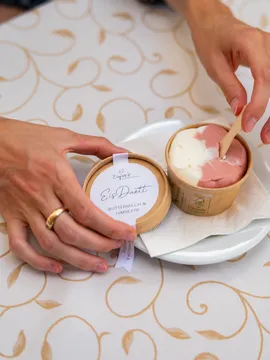Hand opening cup of buttermilk and raspberry ice cream on white plate