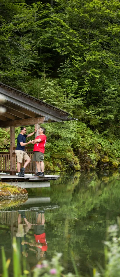 Two men talking on a wooden deck by a forest lake cabin