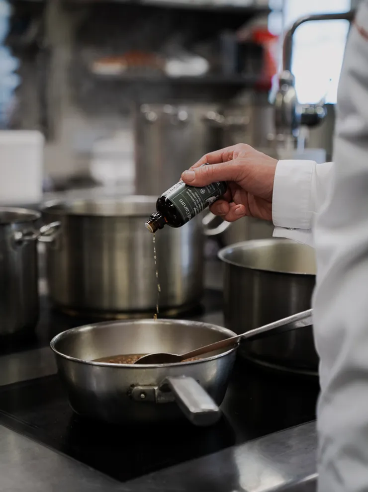 Chef adding liquid seasoning to a saucepan in a professional kitchen