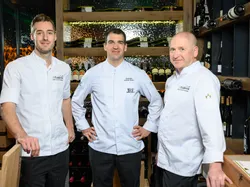 Three chefs in white uniforms standing in a modern wine cellar