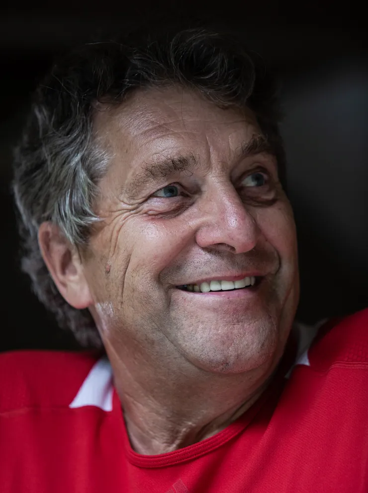 Older man with gray hair smiling and wearing a red Adidas shirt