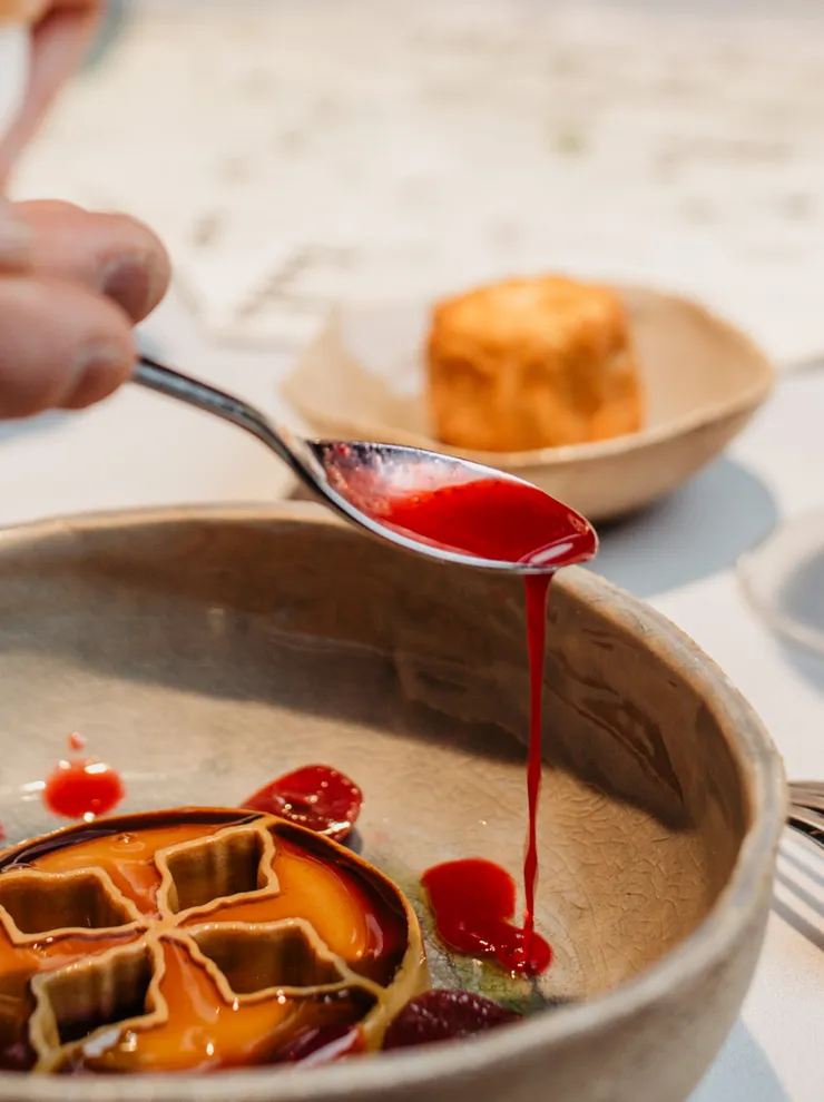 Gourmetgericht mit Beerensauce wird angerichtet, daneben ein Glas Weißwein