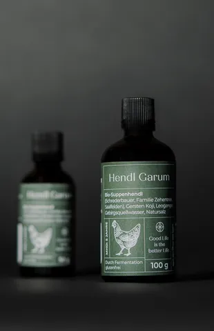 Zwei Flaschen Hendl Garum Hühnerwürzsauce vor dunklem Hintergrund