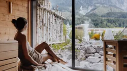 Woman relaxing in sauna with mountain view and outdoor wellness area