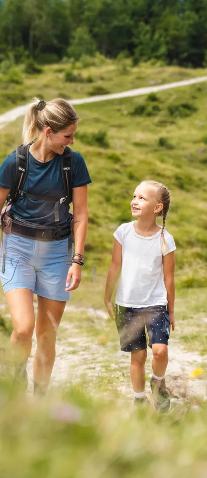 Familie wandert auf Bergpfad durch grüne Wiese an einem sonnigen Tag