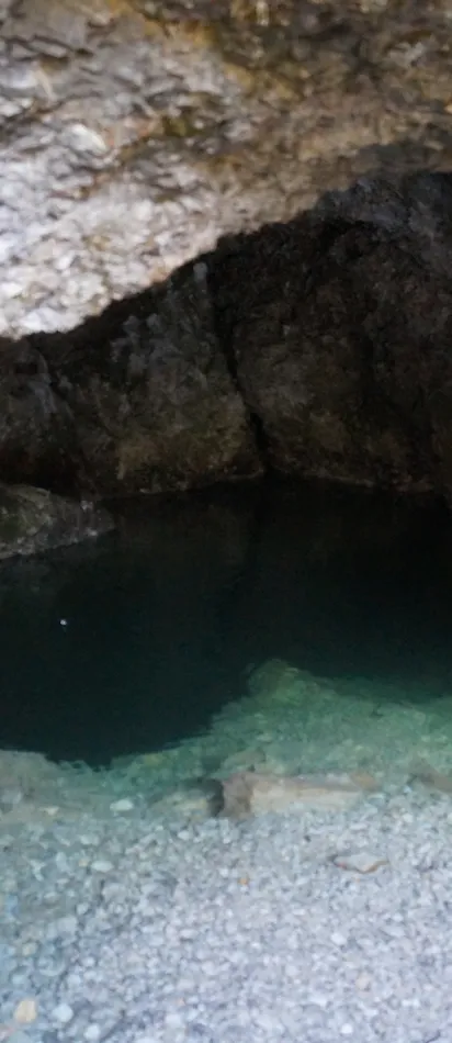 Small crystal-clear pool inside a rocky cave with natural stone walls