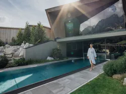 Woman in bathrobe walking by outdoor spa pool at modern alpine wellness resort