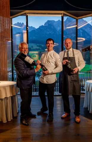 Drei Männer in Gourmetrestaurant mit Weinflaschen und Bergblick im Hintergrund