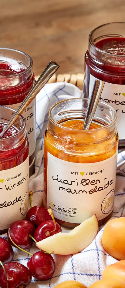 Korb mit verschiedenen Marmeladengläsern und frischem Obst auf einem Küchentuch
