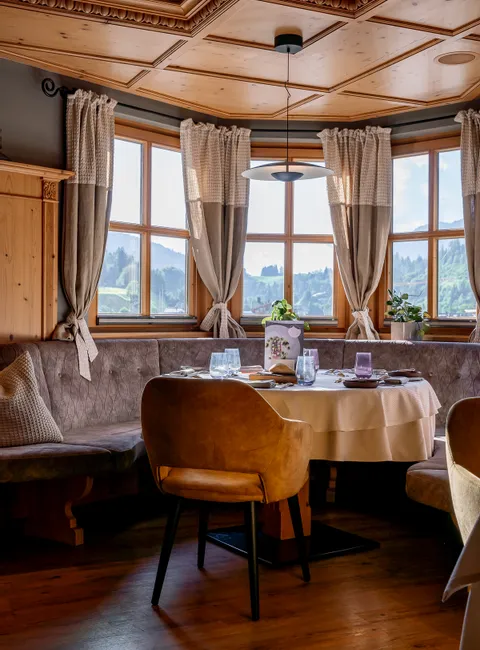 Cozy alpine restaurant corner with wooden ceiling, round table, and panoramic mountain view