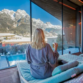 Woman relaxing in spa lounge with mountain view and outdoor pool in winter