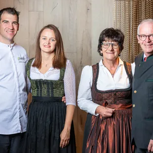 Group of four people in traditional Austrian attire and a chef uniform smiling indoors