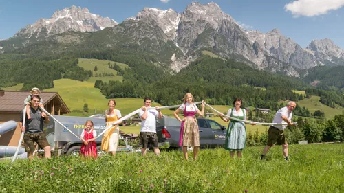 People in traditional Austrian clothing holding a hose in a meadow with alpine mountains in the background