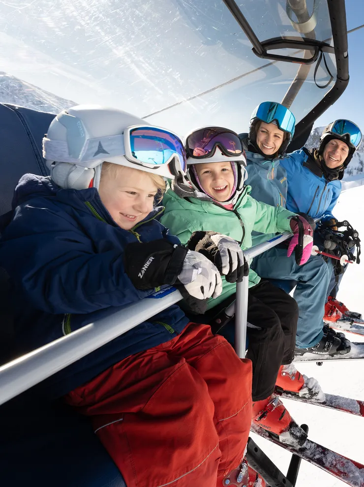 Family with ski gear riding a chairlift in sunny mountain ski resort