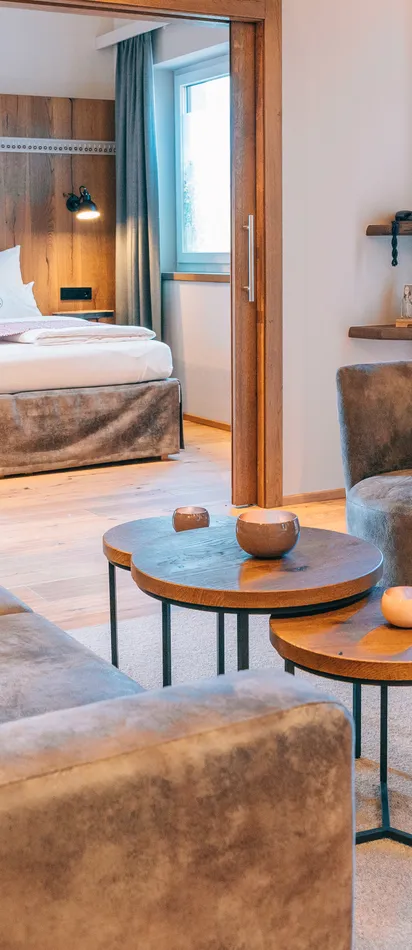 Moderne Hotelsuite mit gemütlicher Sitzecke, runden Tischen und Blick ins Schlafzimmer