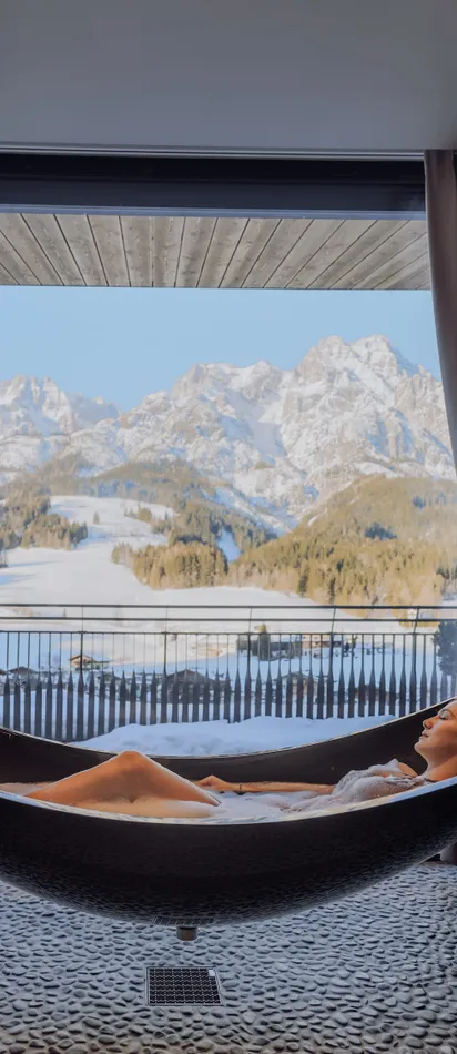 Woman relaxing in a hammock bathtub with snowy mountain view at a luxury spa resort