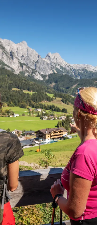 Two women hiking in Leogang with backpacks, overlooking alpine village and scenic mountain range