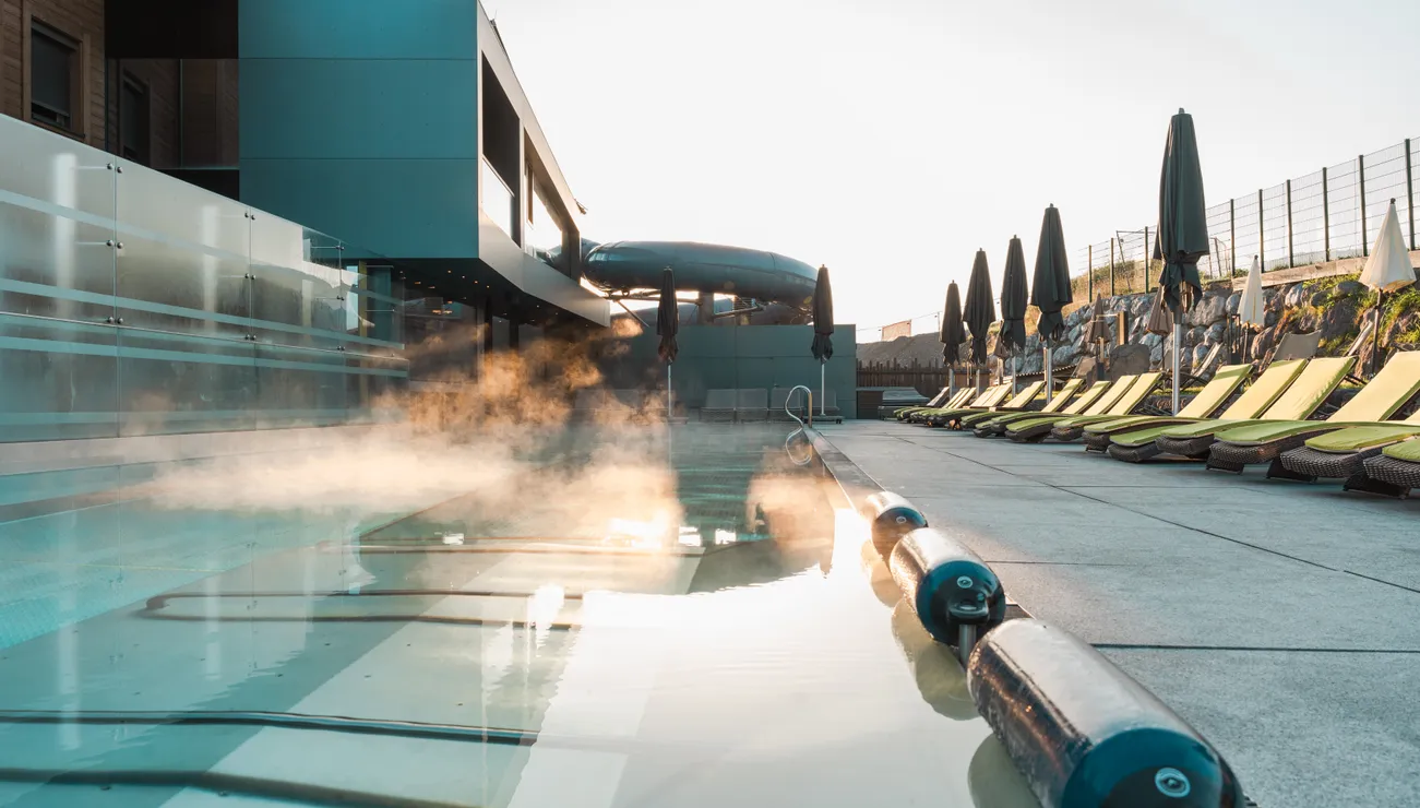 Dampfer auf beheiztem Außenpool neben moderner Hotelterrasse mit Sonnenliegen