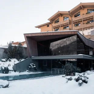 Modernes Alpenhotel mit Außenpool umgeben von Schnee in winterlicher Landschaft
