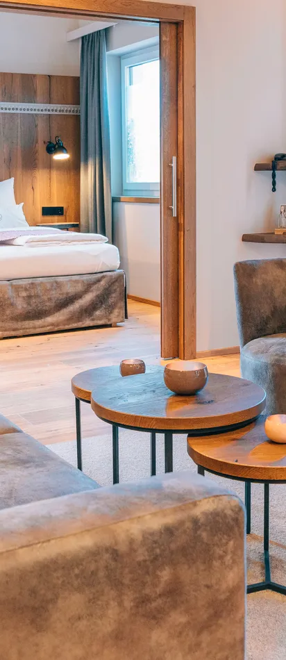 Modern hotel suite with cozy lounge area, round tables and view into the bedroom