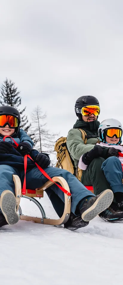 Family sledding down snowy slope with scenic winter mountain background
