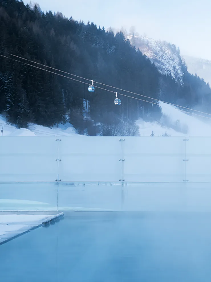 Dampfender Außenpool in einem verschneiten Bergresort mit Seilbahnen im Hintergrund