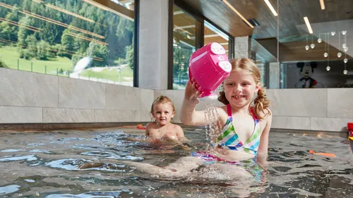Zwei Kinder spielen mit Wasserspielzeug im Innenpool eines Familienhotels in den Alpen