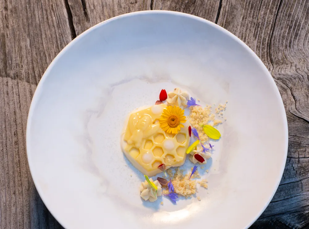 Gourmet-Dessert mit Wabenstruktur und essbaren Blüten auf weißem Teller auf rustikalem Holztisch