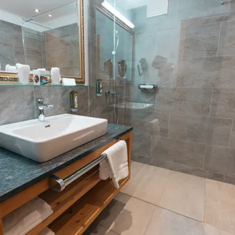 Modern hotel bathroom with sink, mirror, wooden vanity, and glass-enclosed shower