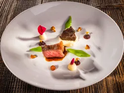 Gourmet-Rindfleischgericht mit Kartoffelpüree, Zuckerschoten und essbaren Blüten auf weißem Teller