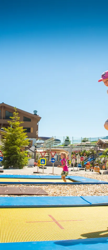 Mädchen springt auf Trampolin bei sonnigem Wetter vor der Riederalm in den Alpen