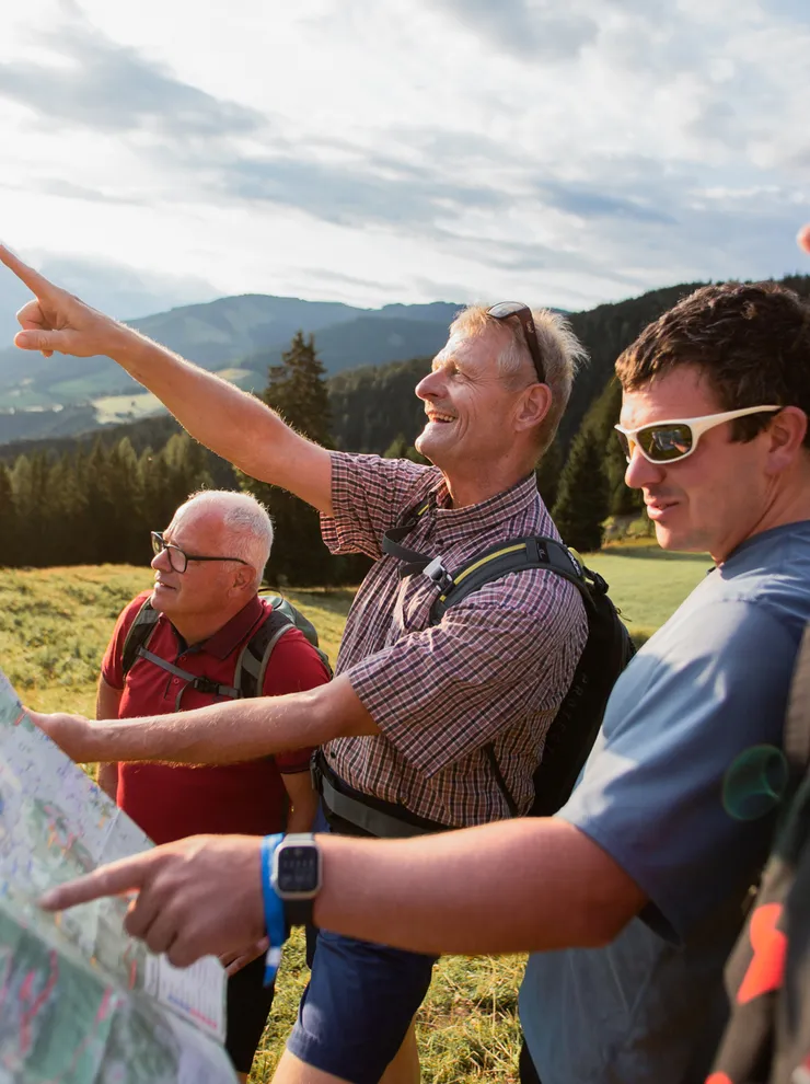 Group of hikers reading a map and pointing toward mountains in scenic alpine landscape