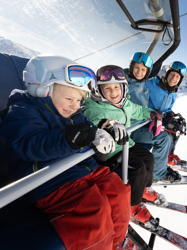 Familie mit Skiausrüstung auf Sessellift im sonnigen Skigebiet